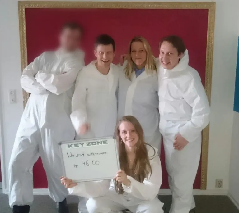 Das Hansolu-Team beim Teambuilding. Michi, Nils, Andrea und Rebecca haben weiße Überzieh-Anzüge an und kommen gerade aus einem Escape-Room. Rebecca hält die Zeit hoch, in der sie entkommen sien (46 Minuten).