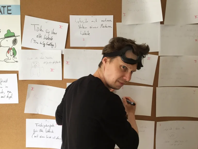 Nils mitten im Kreativmeeting. Er steht an einer Metaplanwand und hat eine Sturmbrille auf dem Kopf.