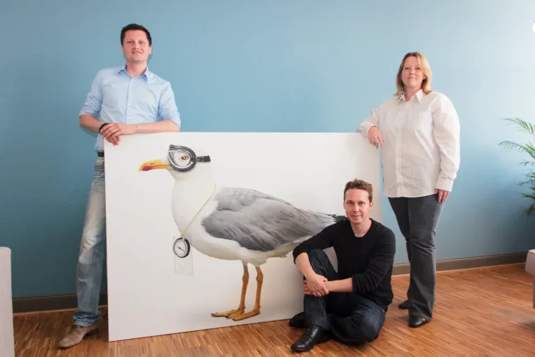 Die Gründer von Hansolu: Patryk, Nils und Andrea. Zwischen Ihnen steht ein großes Bild mit der Hansolu-Möwe darauf.