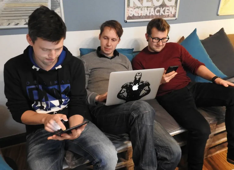 Das Team in der Hansolu-Lounge. Michi, Nils und Fabian sitzen auf einer Couch, die aus Europaletten gebaut wurde. Nils hat einen Laptop vor sich. Michi und Fabi schauen jeweils uaf ein Handy.