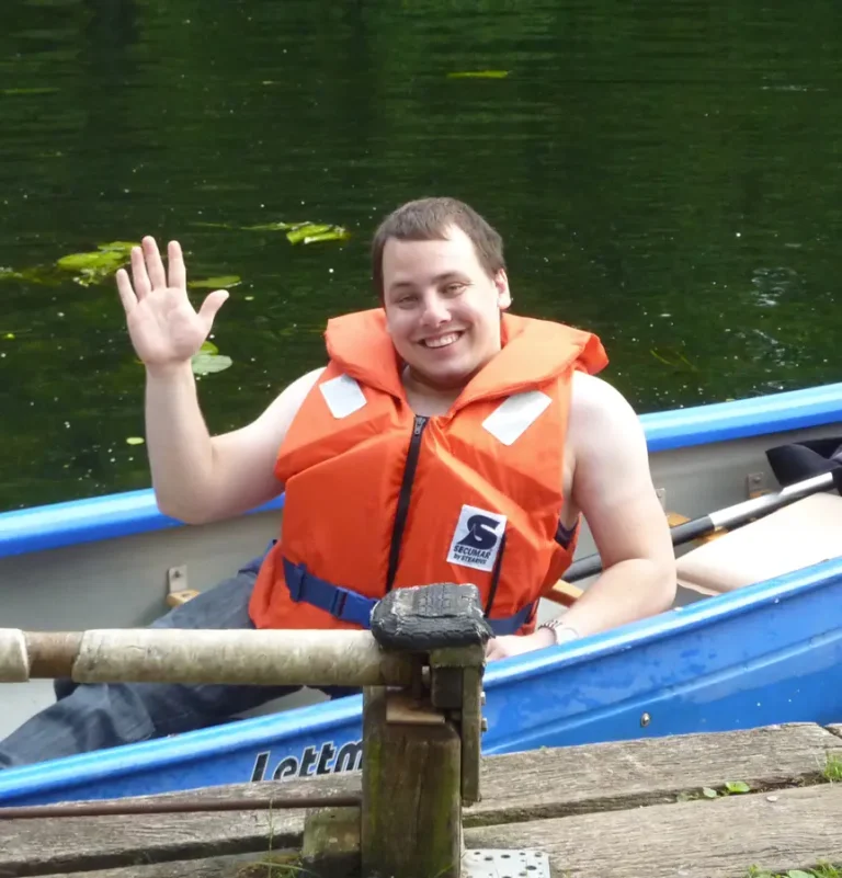 Paul beim Teambuilding. Er sitzt in einem Kanu und winkt.