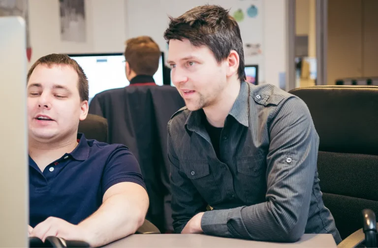 Michi und Paul besprechen etwas und schauen dabei auf einen Monitor.