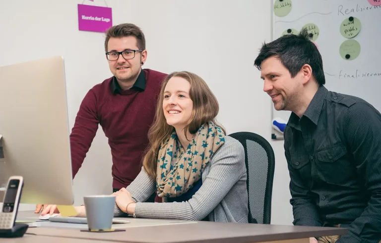 Rebecca, Fabi und Michi schauen sich die Bildergalerie auf einen Bildschirm an einem Arbeitsplatz an.