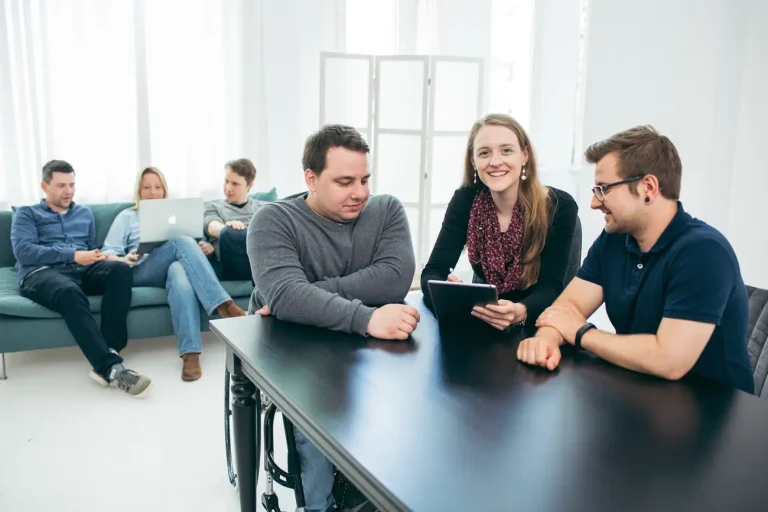 Das Hansolu-Team beim enstpannten Brainstorming. Paul, Rebecca und Fabian schauen gemeinsam auf ein Tablet. Nils, Andrea und Michi sitzen auf einer Couch im Hintergrund und schauen auf eine Laptop.