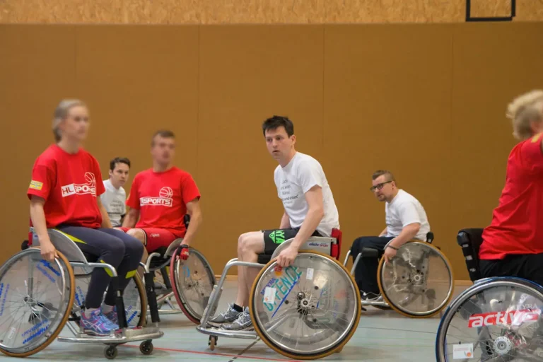 Hansolu beim Rollstuhl-Basketballturnier. Michi sitzt in einem Sportrollstuhl und ist von Gegenspielern umgeben.