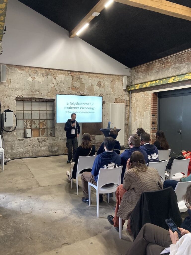 Unser Präsentation auf der IT for Business. Nils steht vor eine Publikum und spricht in ein Mikrofon.