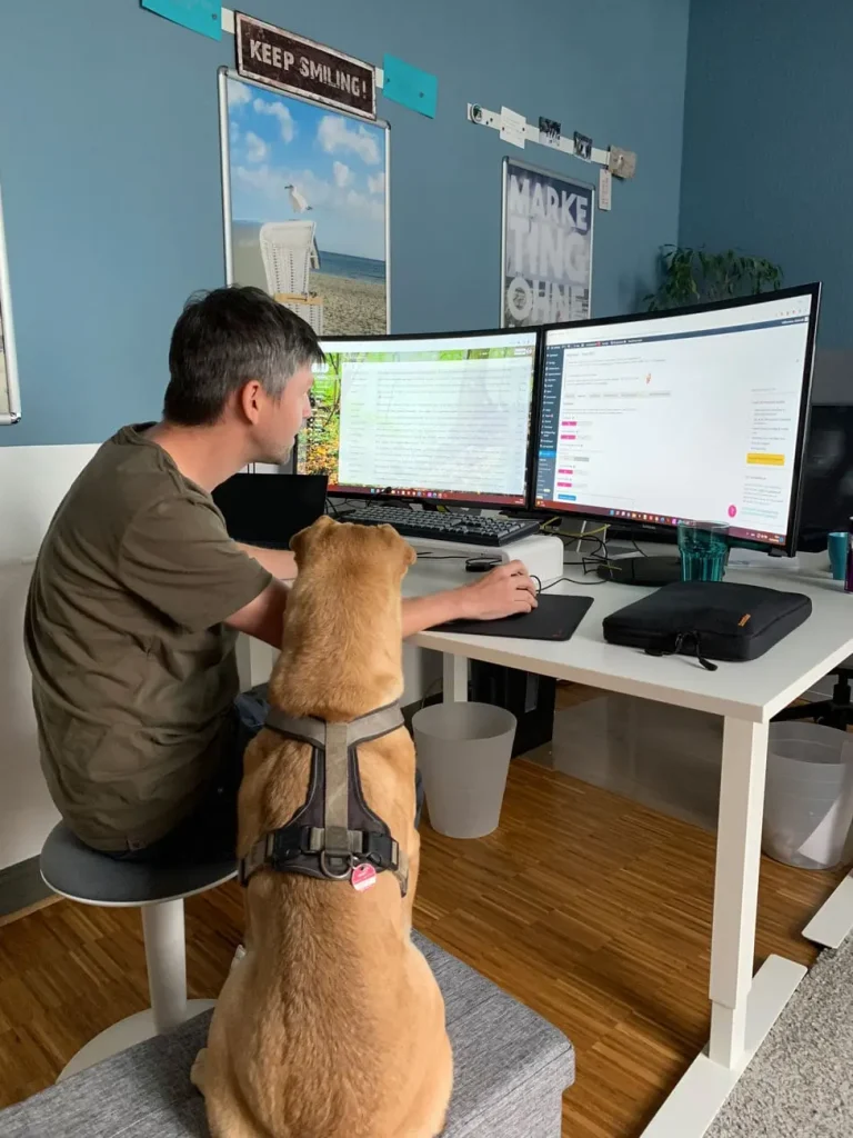 Michi beim Teamwork mit Charly. Charly (unser Bürohund) sitzt neben Michi und schaut mit auf den Monitor.