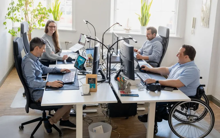 Fabian, Rebecca, Paul und Michi arbeiten gemeinsam an jeweils an einem Schreibtisch im hellen Hansolu-Büro.