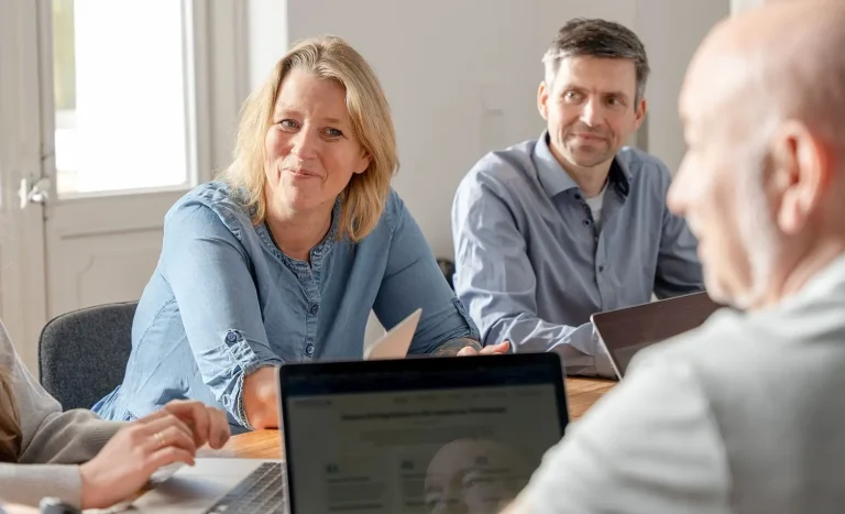 Besprechung im Meetingraum. Man sieht Andrea neben Michi und Alex von hinten.