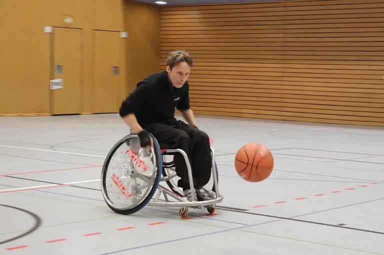 Nils fährt in einem Sportrollstuhl mit konzentriertem Blick einem Basketball nach.