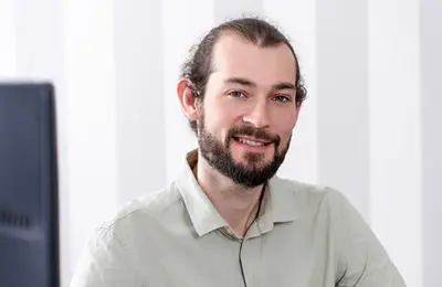 Fabian ist ein Mann mit braunen Haaren. Er trägt ein Hemd und lächelt.